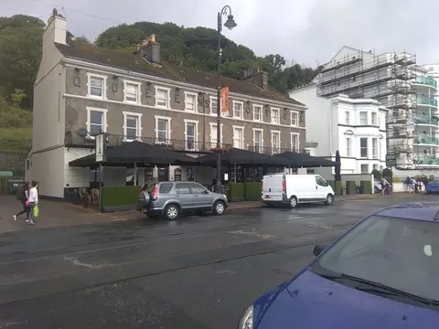 The Queens Hotel from across the promenade road on a wet day, black parasols set out along the front