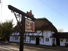 Thatched black-and-white timber-framed pub behind a painted sign of a red lion on an iron post