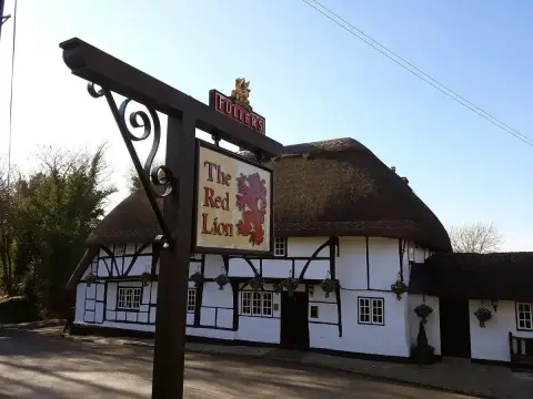 Thatched black-and-white timber-framed pub behind a painted sign of a red lion on an iron post