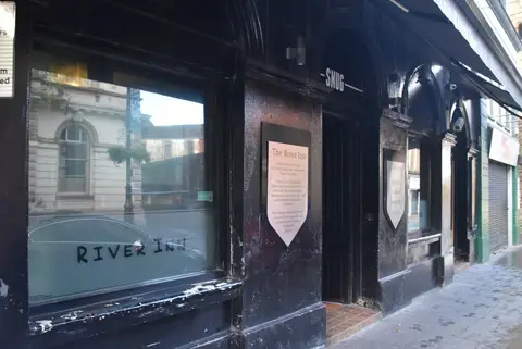Black-painted pub front on Shipquay Street, one window lettered River Inn and a door marked Snug