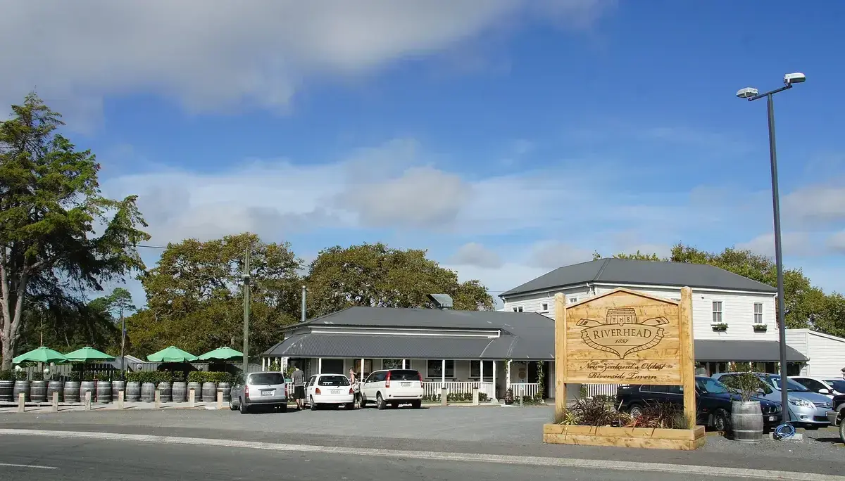White weatherboard tavern with grey roofs and a verandah, behind a carved timber sign and barrels