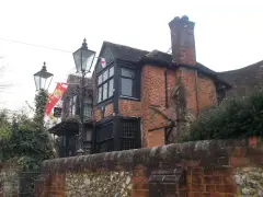 Rambling brick and timber pub with tall chimneys and leaded bay windows above a flint garden wall