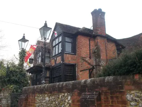 Rambling brick and timber pub with tall chimneys and leaded bay windows above a flint garden wall