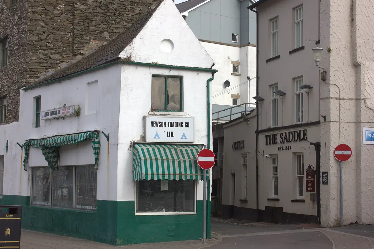 Pub's cream corner elevation lettered The Saddle, est. 1843, beside a closed green and white shop