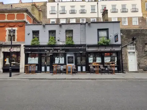 Wider view of the black shopfront pub in a narrow street, grey brick above and Georgian terraces behind