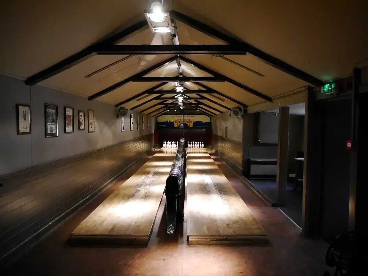 Two long wooden skittle lanes under a beamed roof, pins set at the far end of the hall