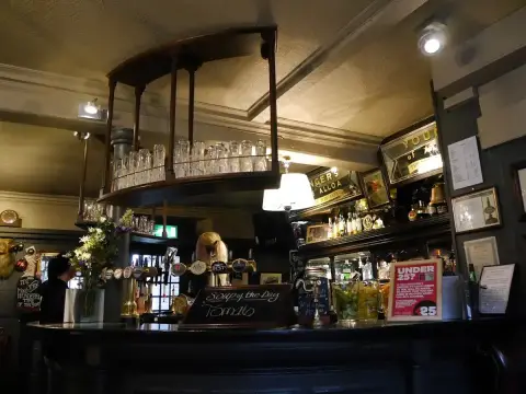 Curved dark-wood bar with a hanging glass rack, brass fonts and old brewery mirrors behind