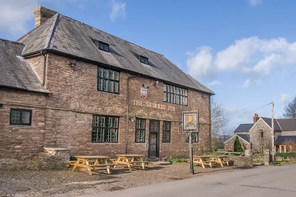 Old red sandstone inn with a steep slate roof, mullioned windows and benches on the cobbles