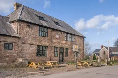 Old red sandstone inn with a steep slate roof, mullioned windows and benches on the cobbles