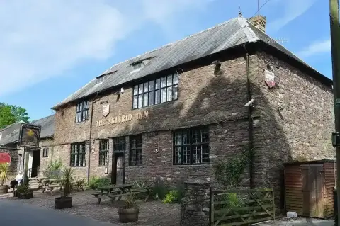 Gable end and front of a rubble-stone inn with gold lettering and a painted hanging sign