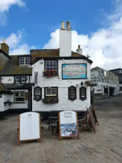 Whitewashed harbour inn with a tall chimney and painted sloop sign, on the cobbled wharf