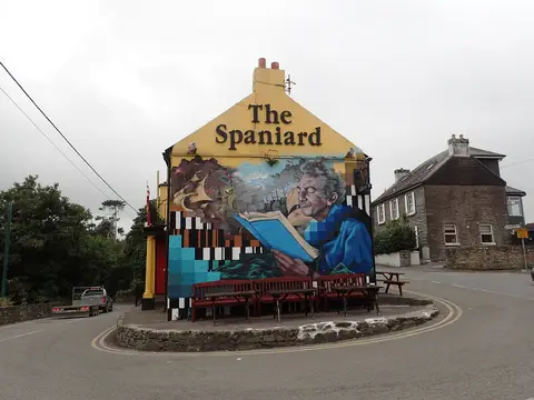 The gable of the Spaniard painted with a mural of ships and a reader, benches beneath