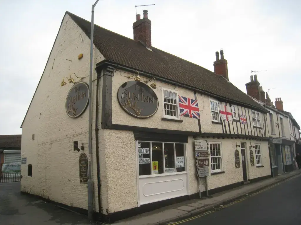 Rendered gable end with two oval name plaques, beside a low timber-framed range on a street corner