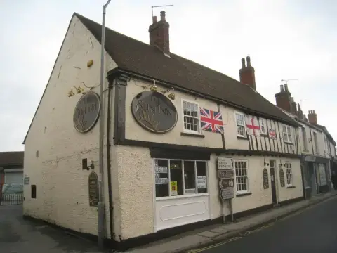 Rendered gable end with two oval name plaques, beside a low timber-framed range on a street corner