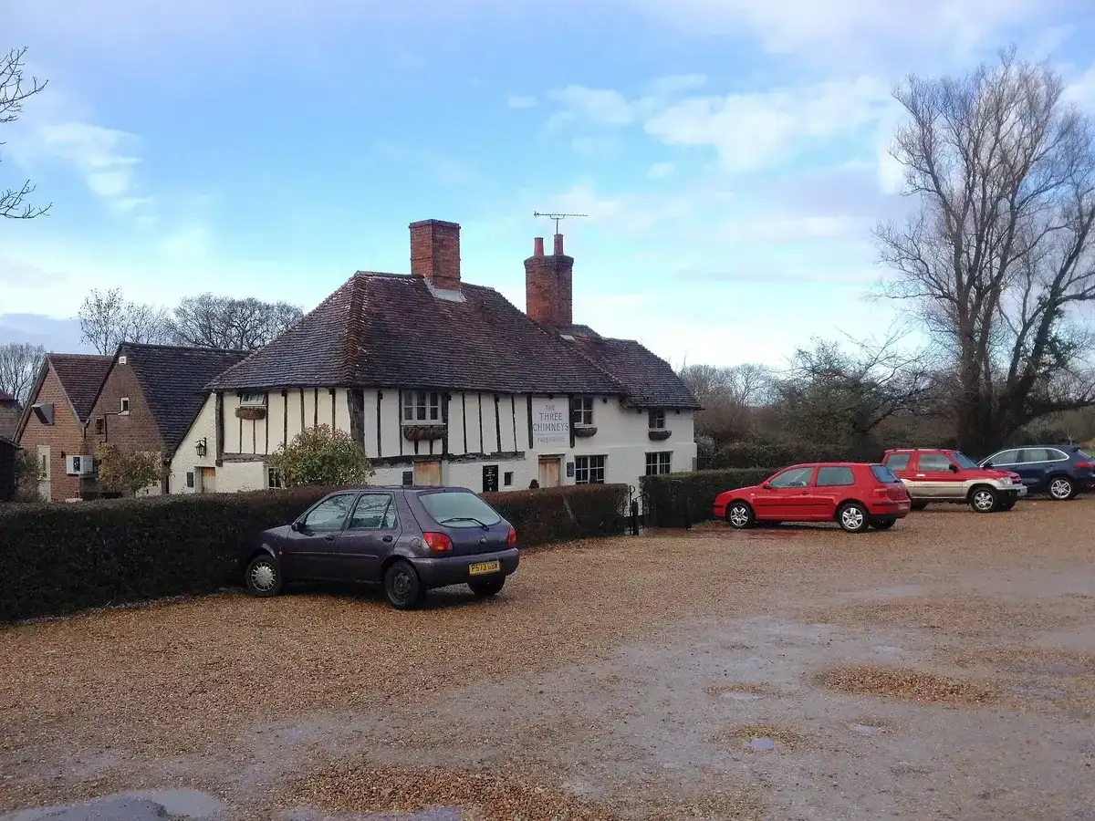 Timber-framed and white-plastered pub with brick chimneys, a name board and gravel forecourt
