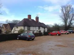 Timber-framed and white-plastered pub with brick chimneys, a name board and gravel forecourt