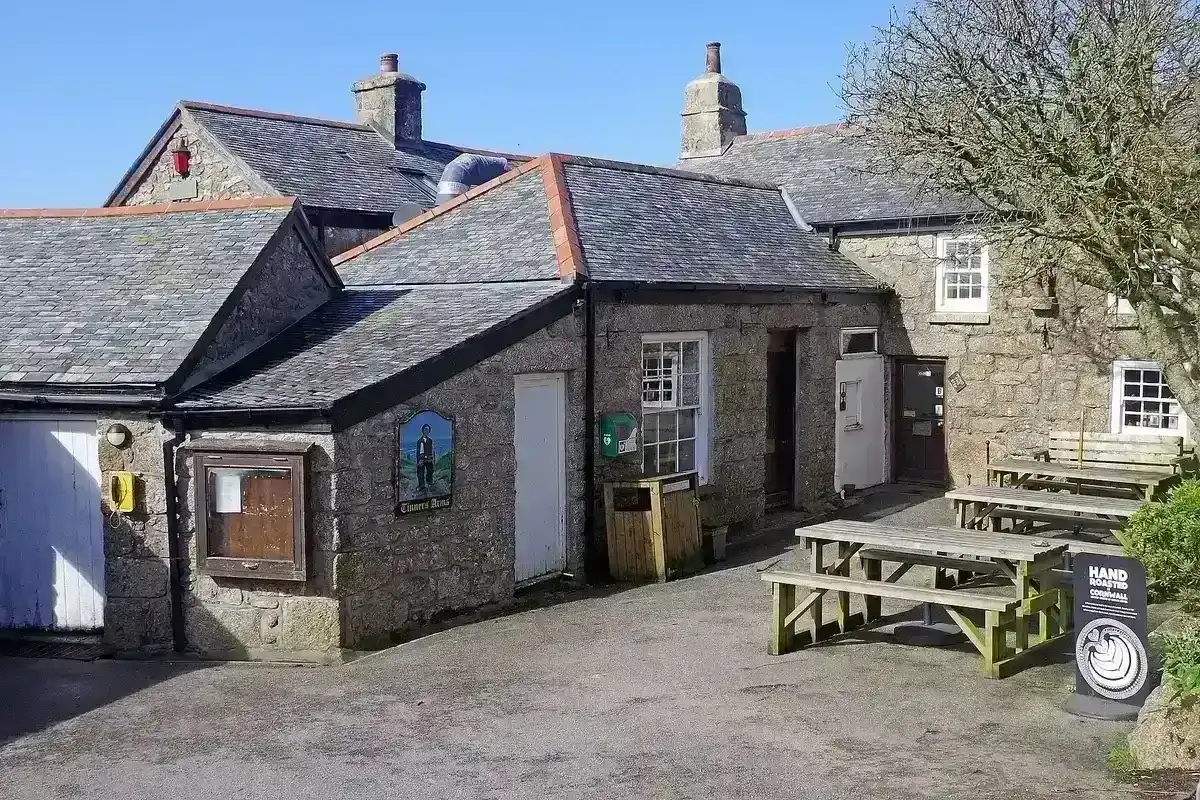 Granite pub with slate roofs around a yard, a painted sign of a tinner beside the door