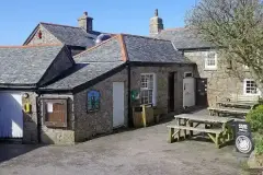 Granite pub with slate roofs around a yard, a painted sign of a tinner beside the door