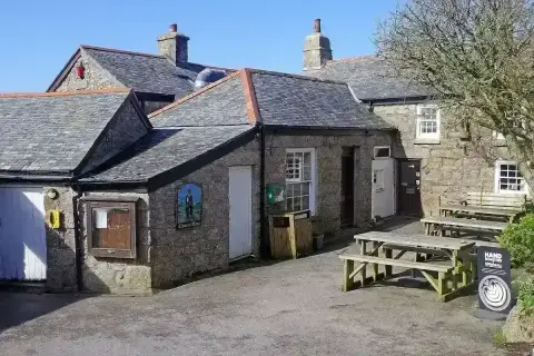 Granite pub with slate roofs around a yard, a painted sign of a tinner beside the door