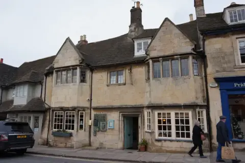 Limestone building with two gables, stone-mullioned windows and a blue door onto the pavement