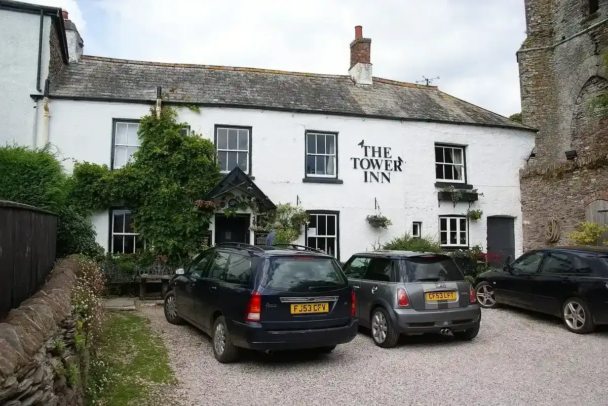 Whitewashed inn with a slate roof and porch, the ruined stone tower rising at the right