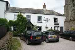 Whitewashed inn with a slate roof and porch, the ruined stone tower rising at the right