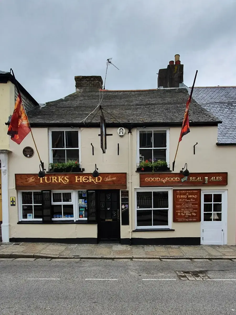 Cream-painted pub front with a carved timber fascia, slate roof and two flags on poles