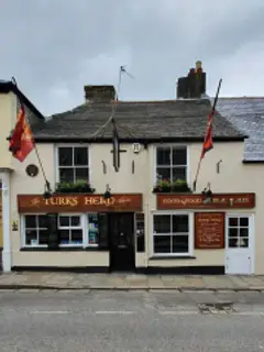Cream-painted pub front with a carved timber fascia, slate roof and two flags on poles