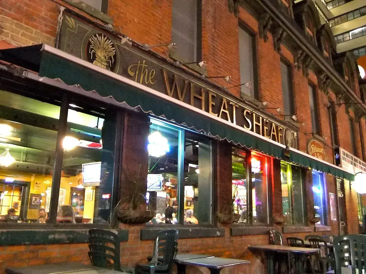 Red-brick tavern front at night with a green awning, gold lettering and a painted wheat sheaf