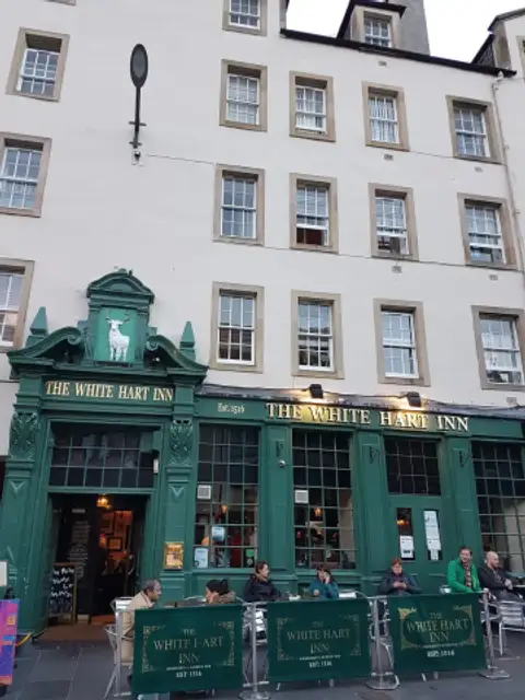 Dark green pub frontage with gold lettering and a white stag over the door, below tenement windows