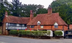 Long tile-hung and timber-framed pub behind a clipped hedge, brick stacks and red parasols
