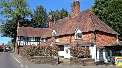 Tile-hung pub in bright sun with photinia hedging in front and its timber-framed end to the road