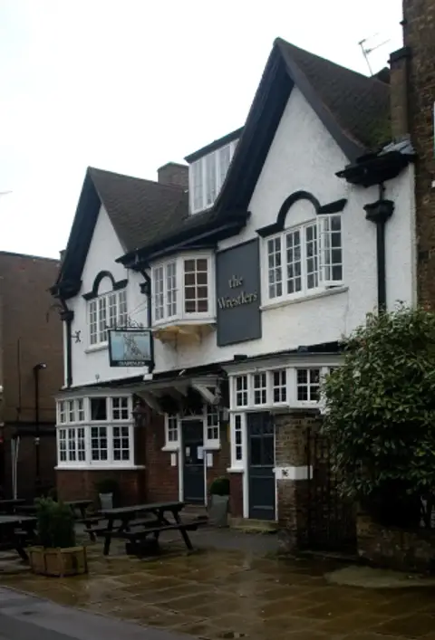 White roughcast pub with gabled dormers, bay windows and a painted sign, benches on the paving