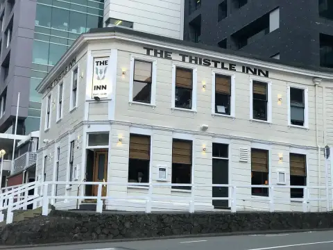 Cream weatherboard corner inn with its name in black capitals, hemmed in by glass office towers