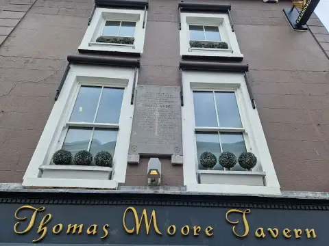 A tavern front in gold script lettering reading Thomas Moore Tavern, with a stone plaque set in the wall above it between sash windows
