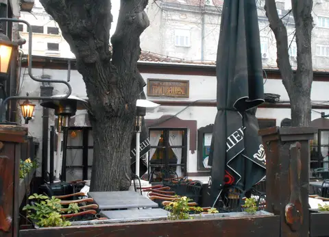 Terrace with heaters and furled parasols in front of a low white house, a carved name-board above
