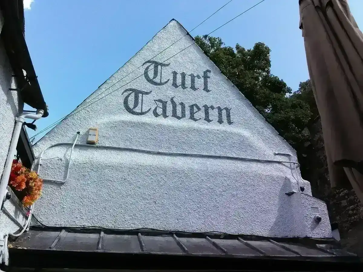 White rendered gable painted with the tavern's name in black blackletter, above a tiled roof