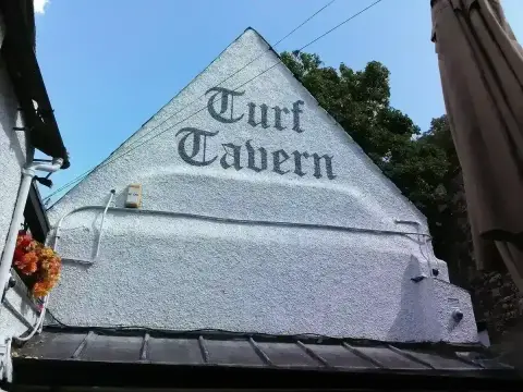 White rendered gable painted with the tavern's name in black blackletter, above a tiled roof