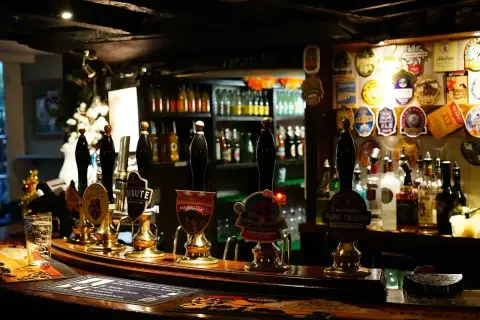 Curved bar counter with a row of handpumps under a low beamed ceiling hung with pump clips