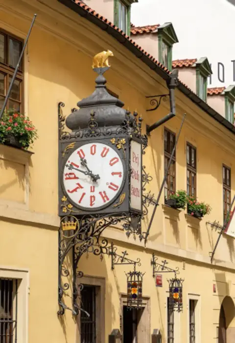 Ornate ironwork clock with red blackletter numerals and a gilded bear, on a yellow wall