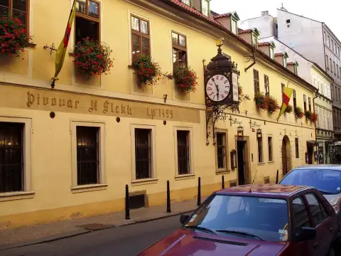 Yellow rendered brewery frontage lettered Pivovar U Fleku 1499, with window boxes and a clock