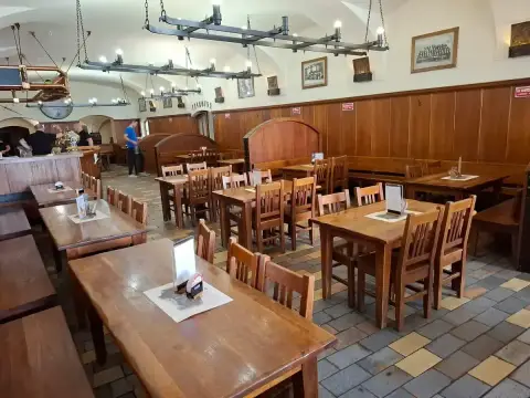 Long vaulted beer hall with plain wooden tables and benches and iron candle-beam lights
