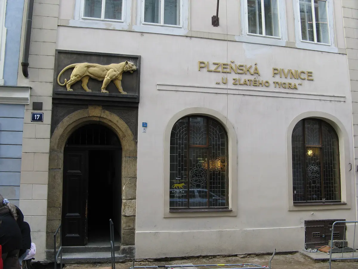 Pale frontage with a golden tiger relief over an arched door and gold lettering U zlatého tygra