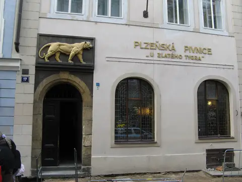 Pale frontage with a golden tiger relief over an arched door and gold lettering U zlatého tygra