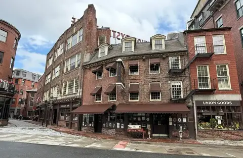 Brick house of three storeys with dormers and brown awnings, on a cobbled corner of the Blackstone Block