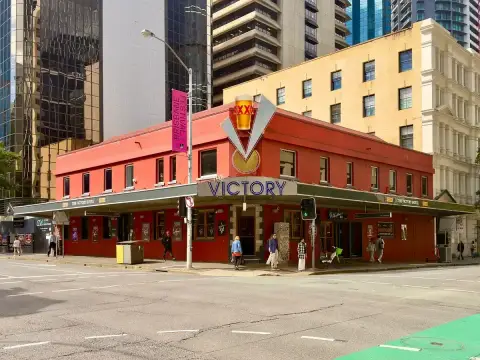 The same corner in sun, a beer-glass sign on the roof and people on the footpath below
