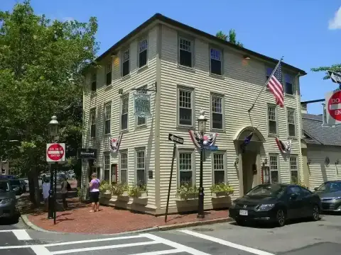 Three-storey cream clapboard tavern on a corner with a hanging sign, flag and window boxes