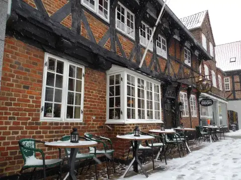 Brick and timber front in falling snow, green café tables outside and a hanging Weis Stue sign