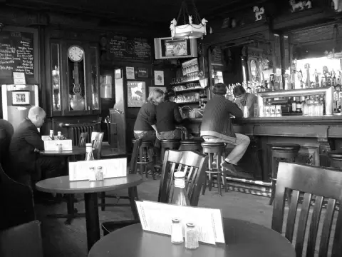 Dark timber bar with a long mahogany counter, tall clock, chalkboards and bentwood chairs