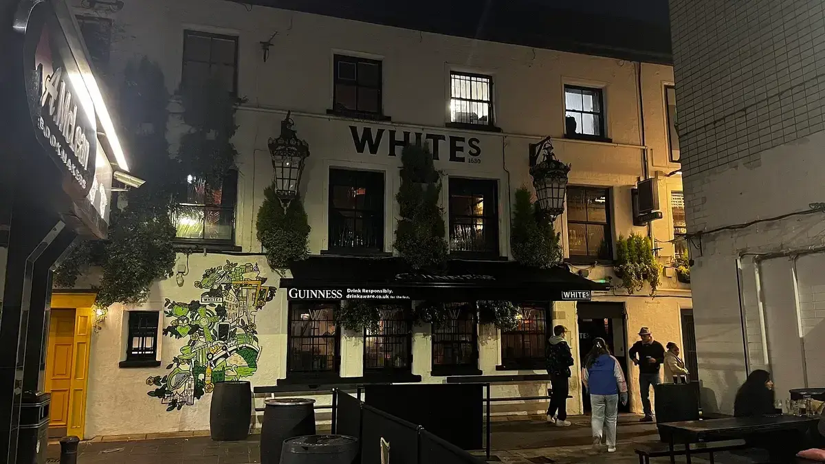 White-painted tavern front at night, lit lanterns either side of large black-framed windows